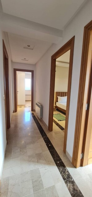 Ein Korridor, der in ein Schlafzimmer mit Bett, Heizkörper und Fenster führt.