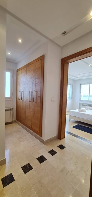 A hallway with a wooden wardrobe, a radiator, and a tiled floor with black squares. - Luxurious 3-bedroom Apartment in Heart of Tunis (Tunis)