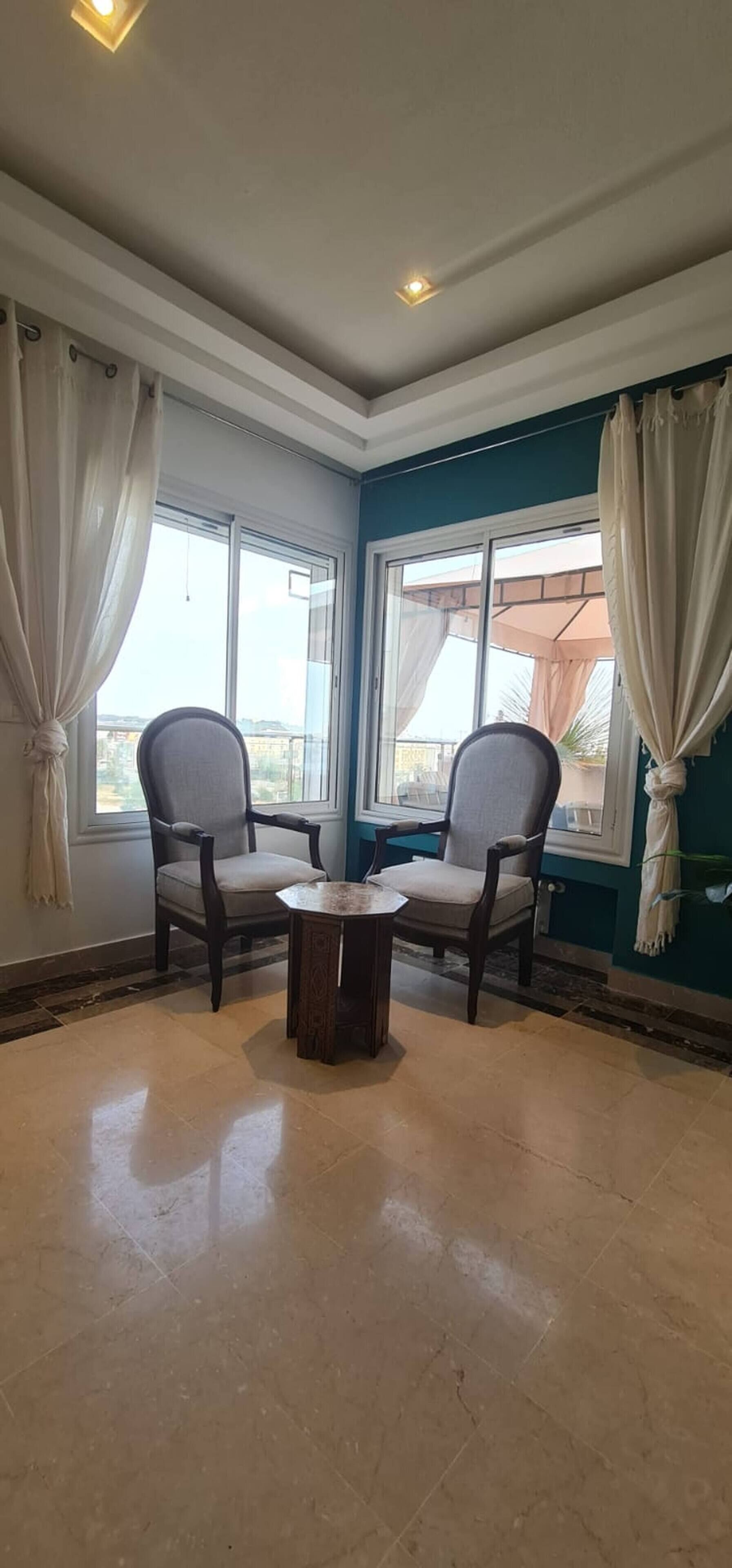 Une pièce avec deux chaises, une petite table et de grandes fenêtres avec des rideaux.