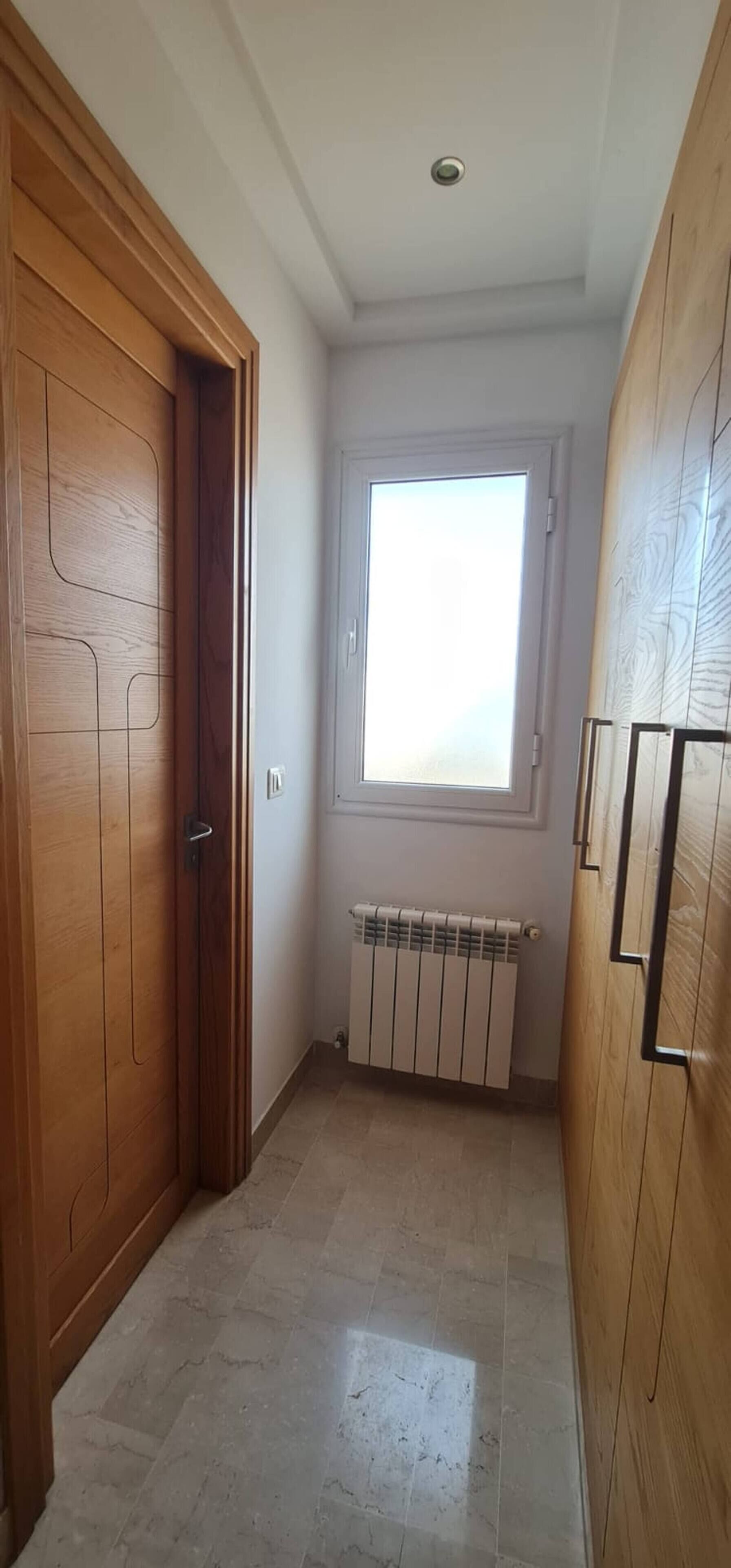 Passadís amb una porta de fusta, un radiador i una finestra.