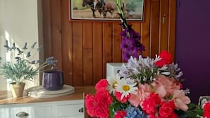 A dining area with a floral tablecloth, a vase of flowers, a wooden wall with a framed picture, and a purple door. - Guesthouse Room for 2 or 3 – Breakfast Included (Priziac)