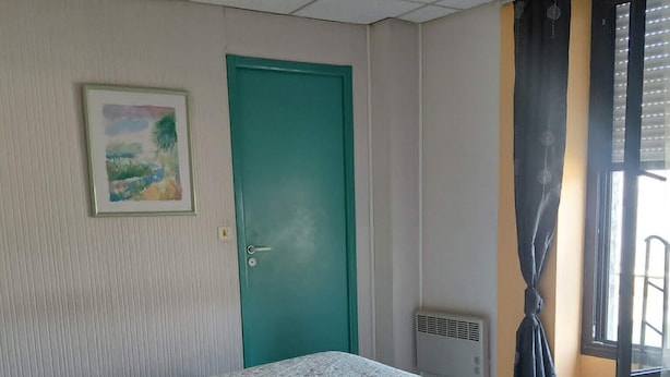 A room with a bed, a door, a radiator, and a window with curtains. - Guesthouse Room for 2 or 3 – Breakfast Included (Priziac)