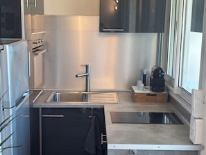 A modern kitchen with stainless steel appliances, a sink, and a window providing natural light. - 30-square-meter apartment ideally located on the waterfront (Fréjus)