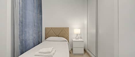 Een hotelkamer met een bed, nachtkastje, lamp en een raam met gordijnen.