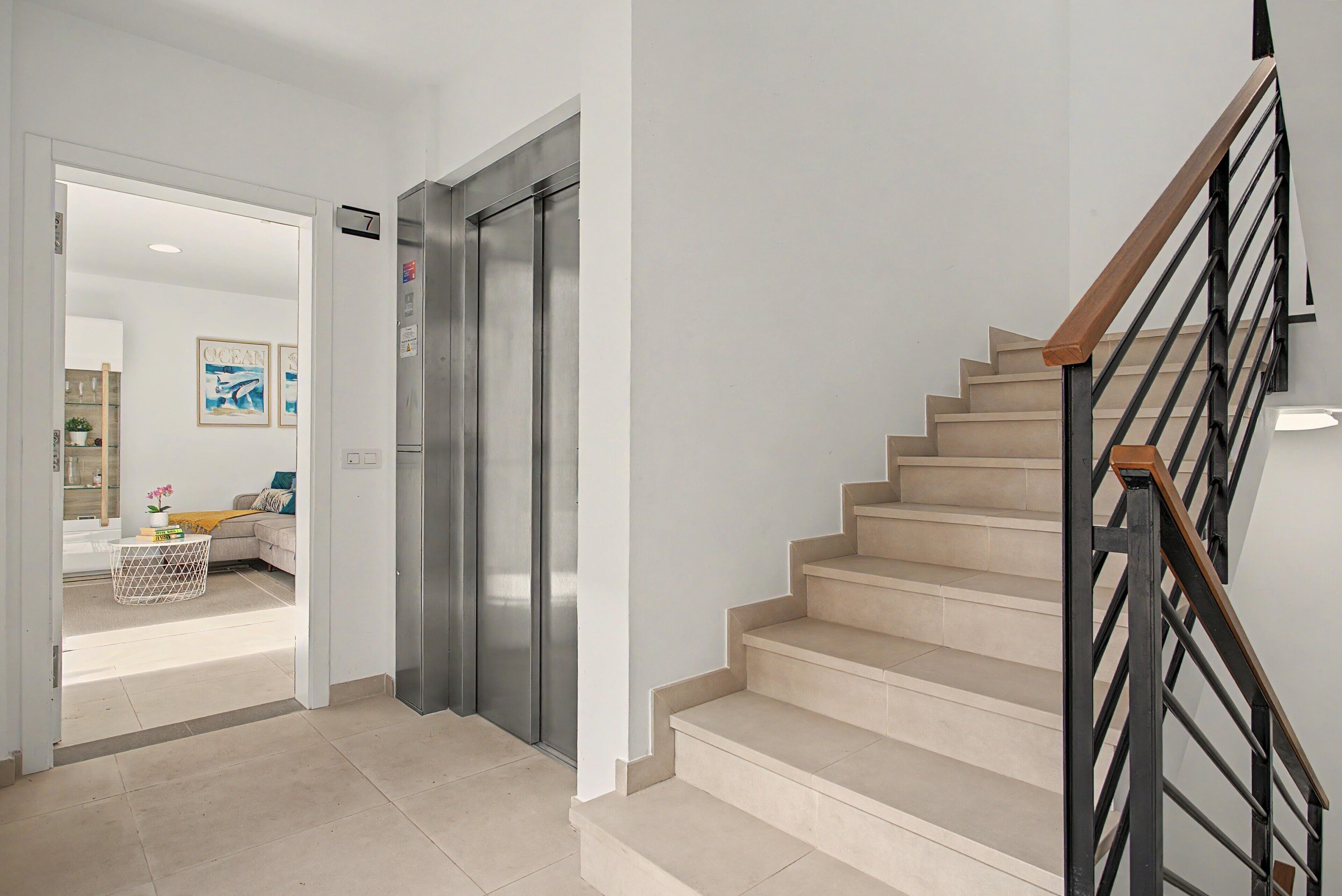 A modern interior with a staircase, a door leading to a living area, and a stainless steel elevator.