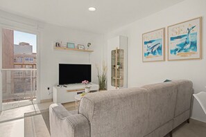 A modern living room with a flat-screen TV, a grey sofa, and two framed ocean-themed artworks. - Vacation Apartment 'Brisa C' with Balcony, Wi-Fi and Air Conditioning (El Médano)