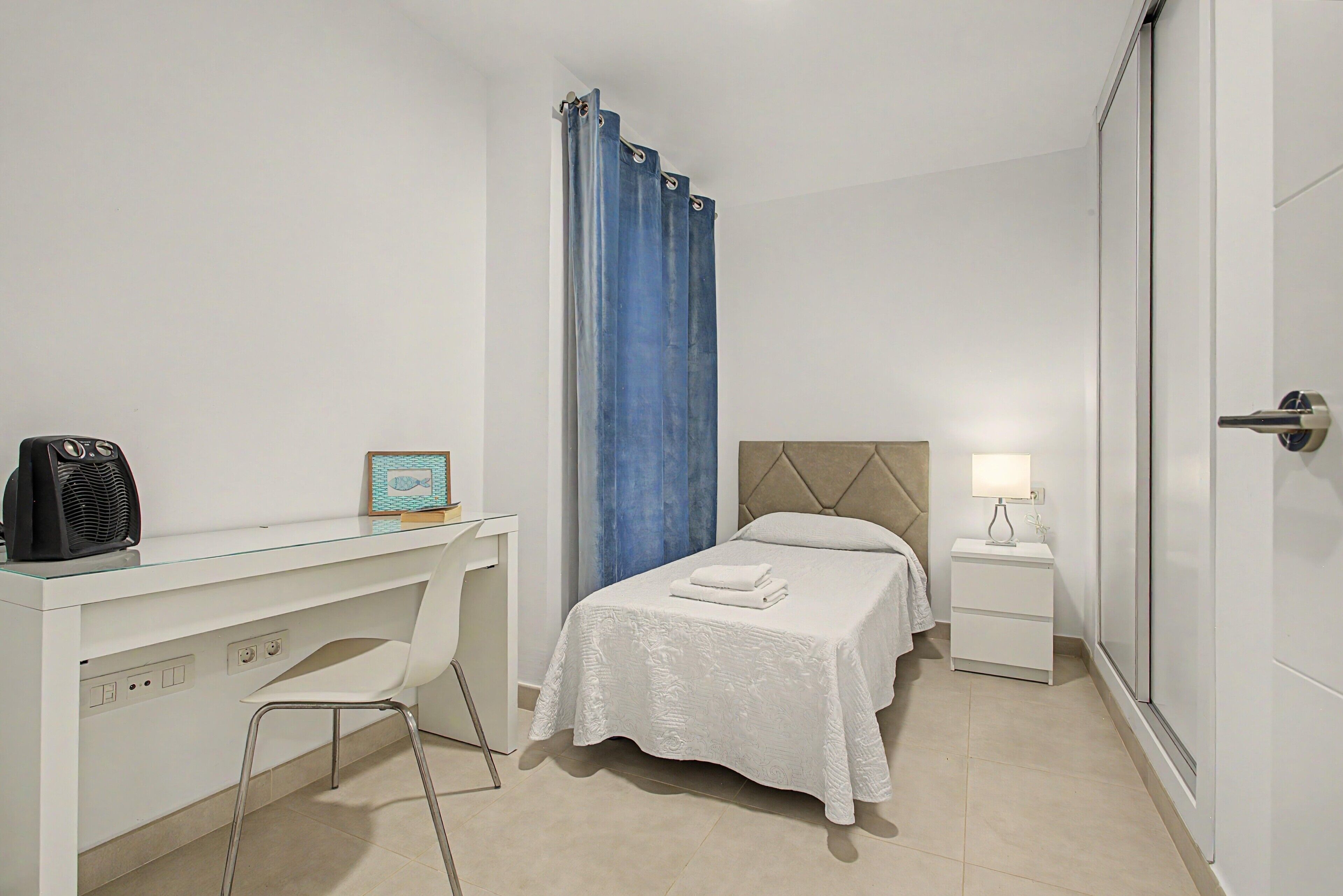 Een hotelkamer met een bed, een bureau met stoel, een nachtkastje met lamp en een kledingkast.