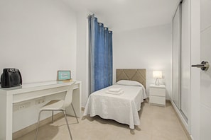 A hotel room with a bed, a desk with a chair, a bedside table with a lamp, and a wardrobe. - Vacation Apartment 'Brisa C' with Balcony, Wi-Fi and Air Conditioning (El Médano)
