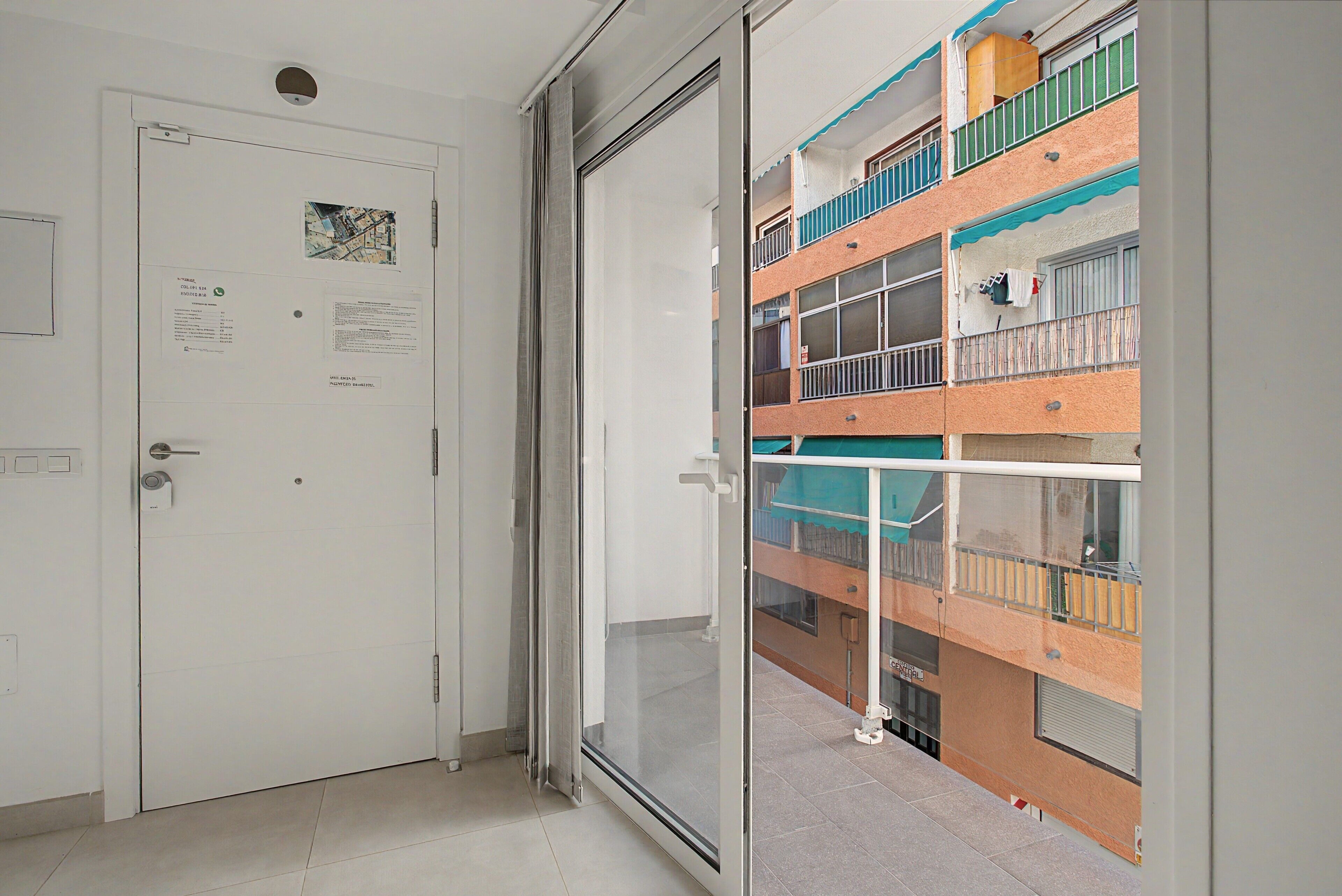 Ein Zimmer mit einer Schiebetür zu einem Balkon mit Blick auf ein mehrstöckiges Gebäude.