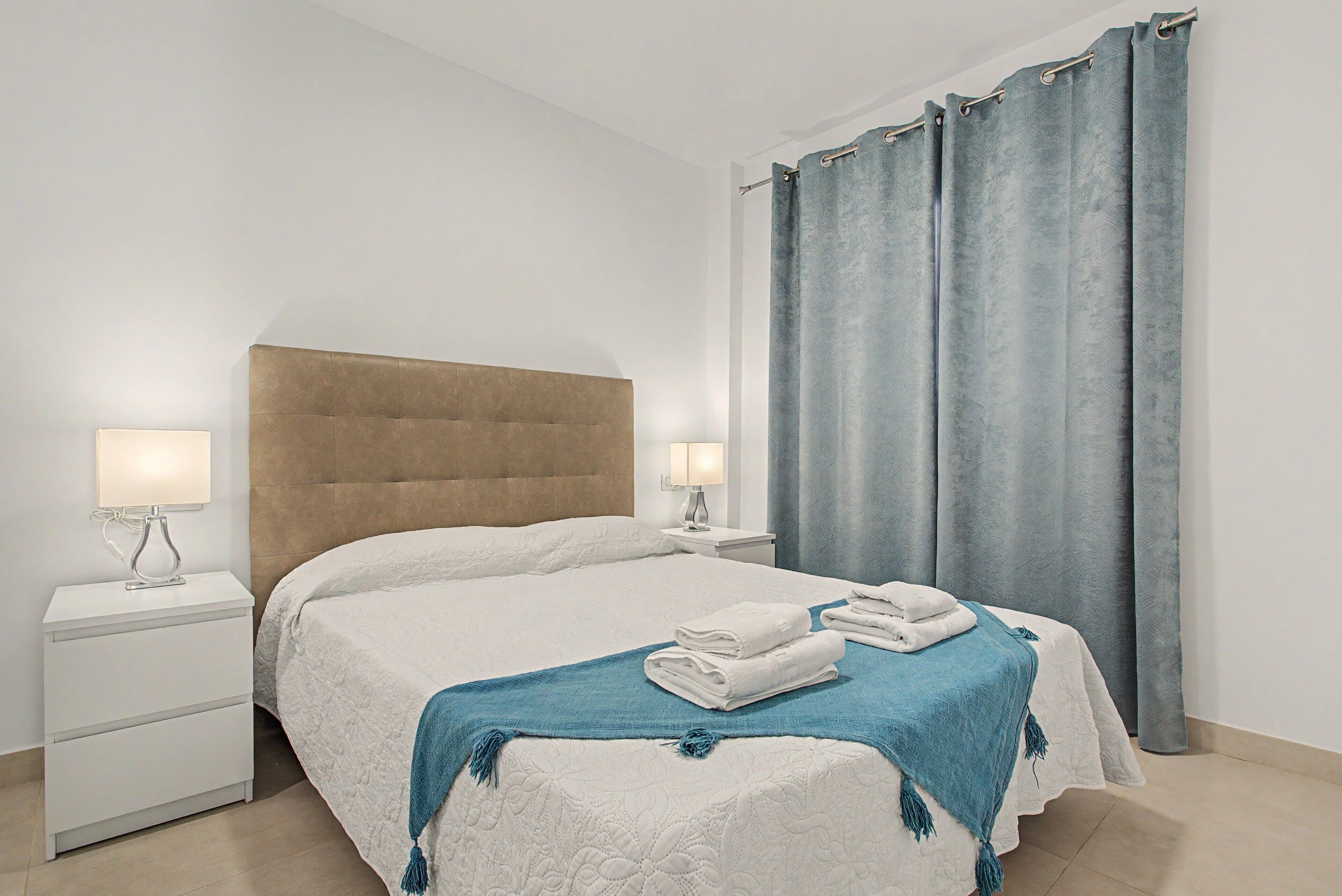 A hotel room with a large bed, two bedside tables with lamps, a headboard, and a window with curtains.