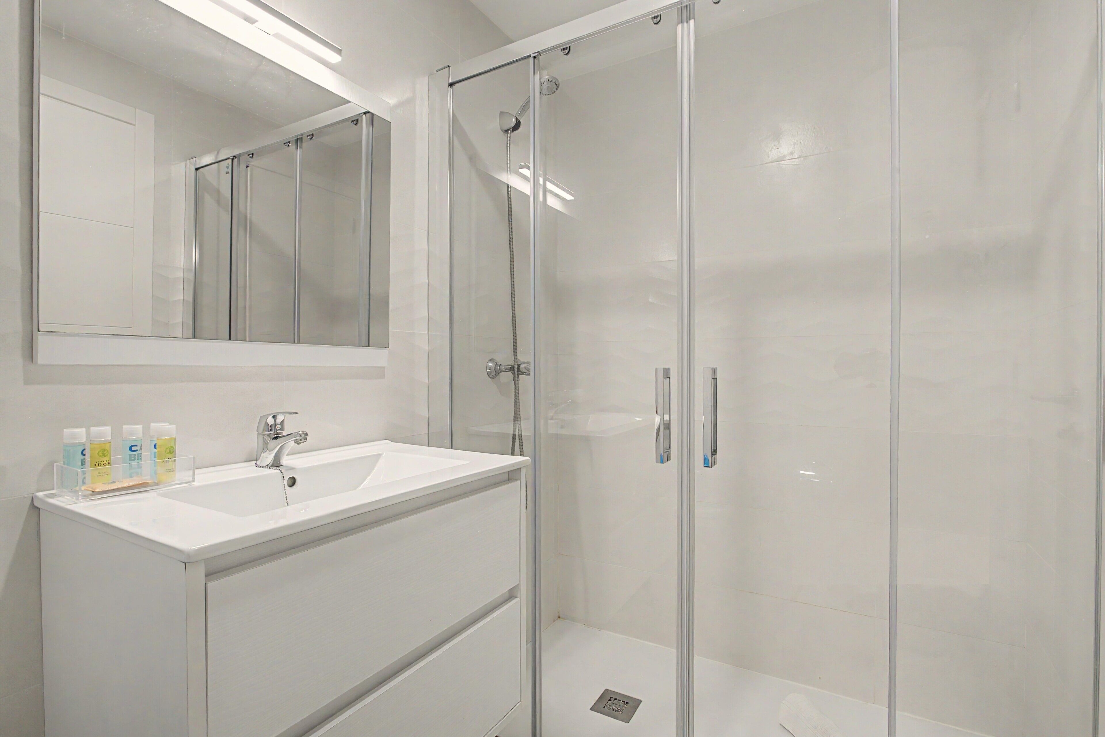 Une salle de bain moderne avec une douche à parois de verre, un lavabo blanc et un miroir au-dessus.