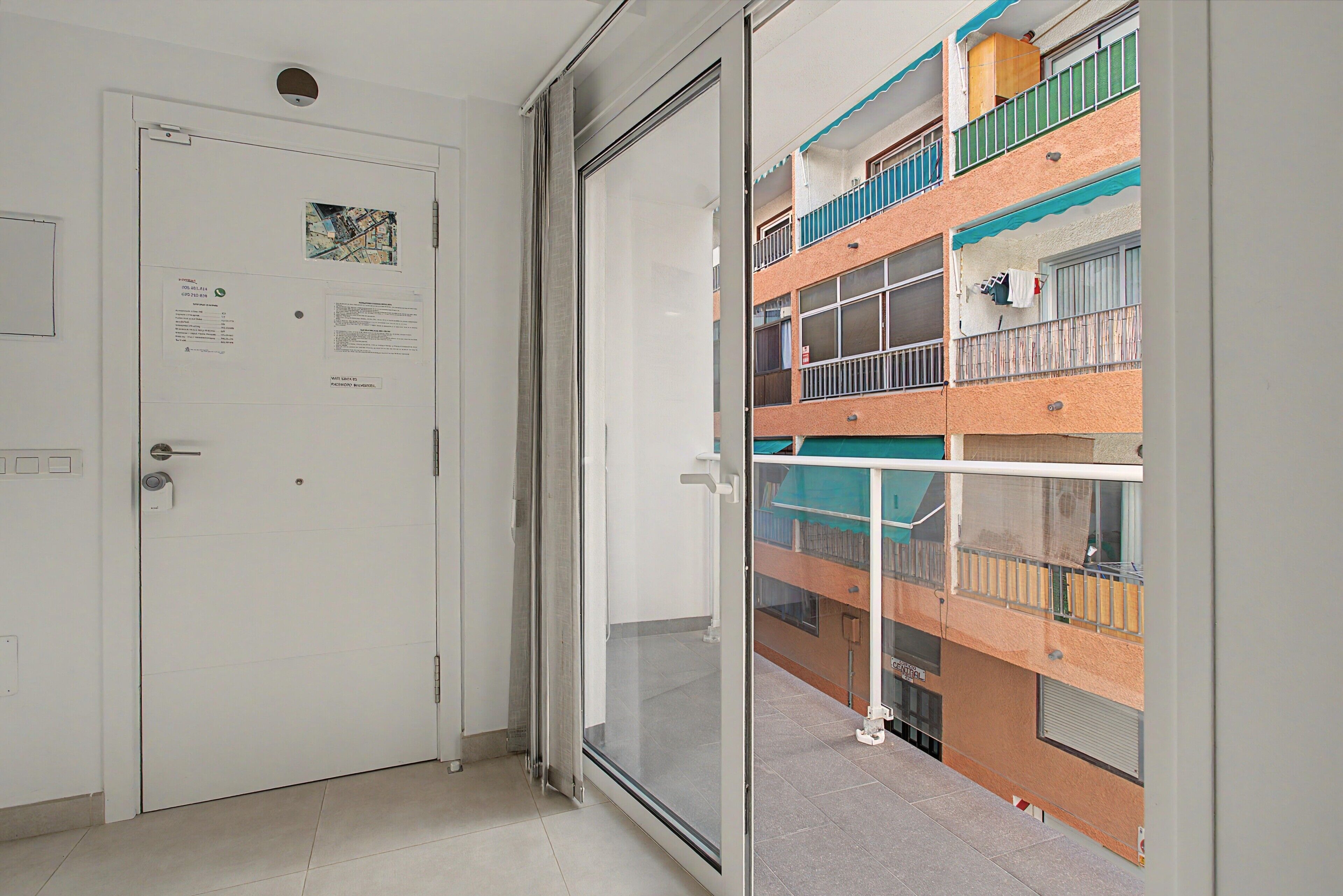 A room with a sliding glass door leading to a balcony with a view of a multi-story building.