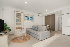 Una sala de estar moderna con un sofá gris, una mesita redonda, una estantería y dos cuadros colgados en la pared.