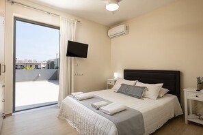 A hotel room with a bed, a TV, an air conditioner, a nightstand, and a view of the outside. - Hestia Grey Barefoot Escape 100m From Beach (Rethymno)