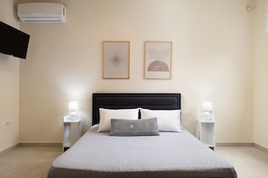 A bedroom with a bed, two bedside tables with lamps, an air conditioner, and two framed artworks on the wall. - Hestia Grey Barefoot Escape 100m From Beach (Rethymno)