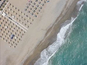 An aerial view of a beach with rows of sun umbrellas and beach chairs, a walkway, and the ocean. - Hestia Grey Barefoot Escape 100m From Beach (Rethymno)
