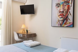 Une chambre d’hôtel avec un lit, un bureau doté d’une lampe, un téléviseur fixé au mur et un tableau.