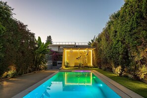 Une piscine au design moderne, entourée de haies bien entretenues et sous un ciel dégagé.