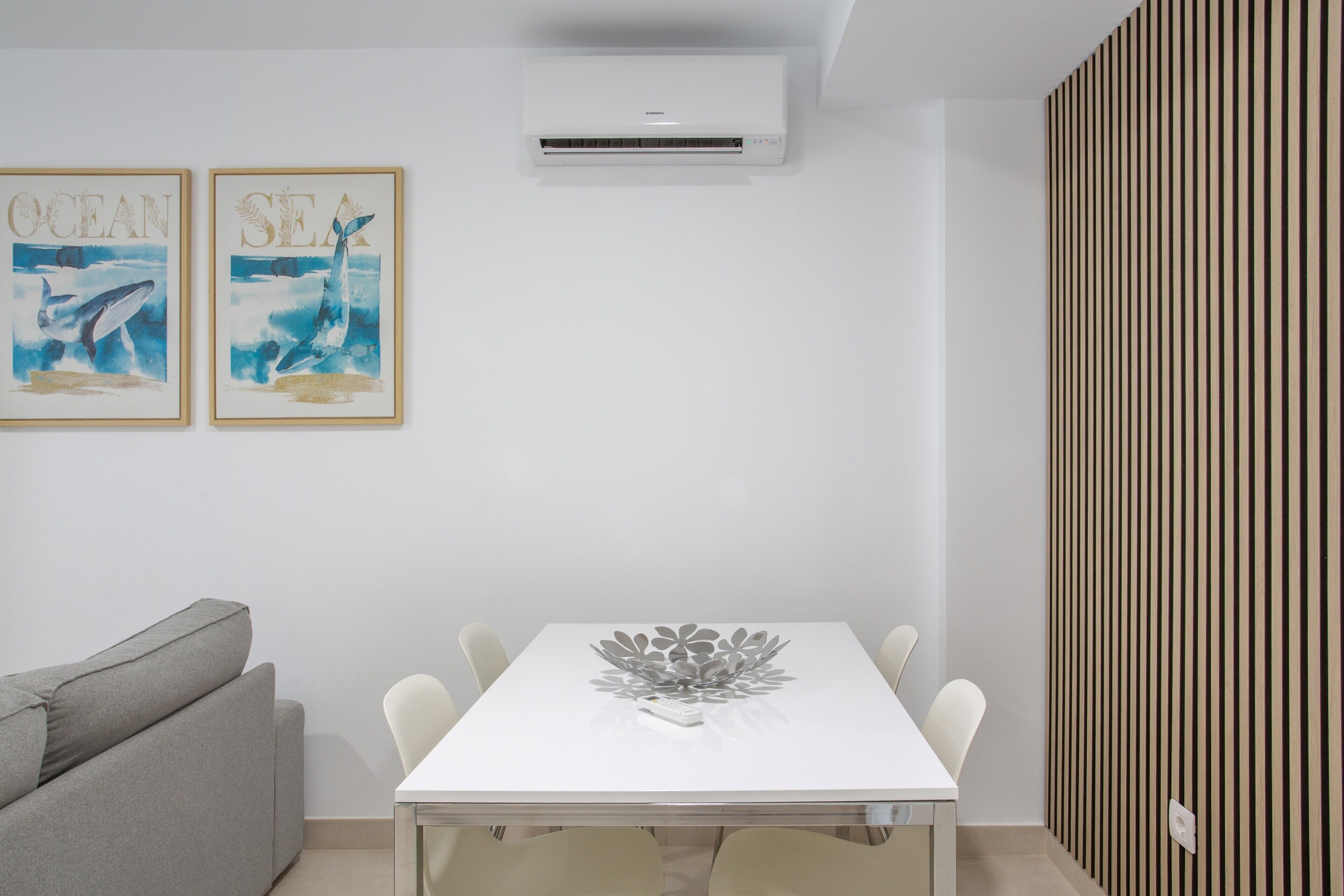 Habitación moderna con una mesa blanca, sofá gris y dos cuadros enmarcados que representan vida marina.