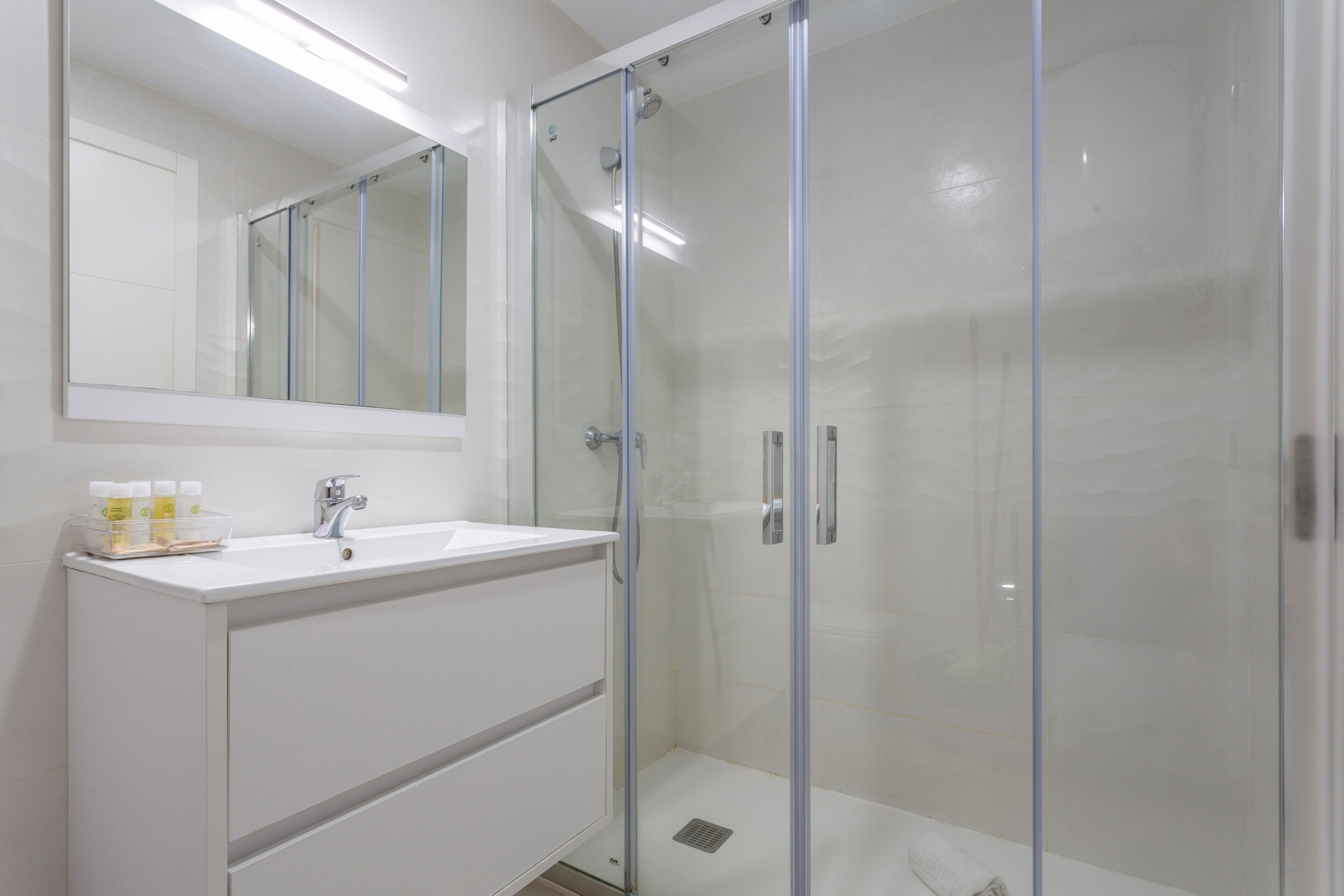Un bagno moderno con cabina doccia in vetro, un lavandino bianco e uno specchio sopra il mobile.