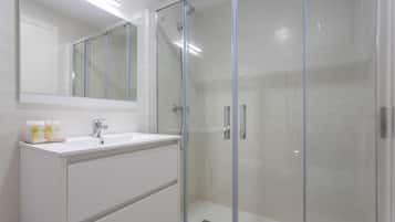 Un bagno moderno con cabina doccia in vetro, un lavandino bianco e uno specchio sopra il mobile.