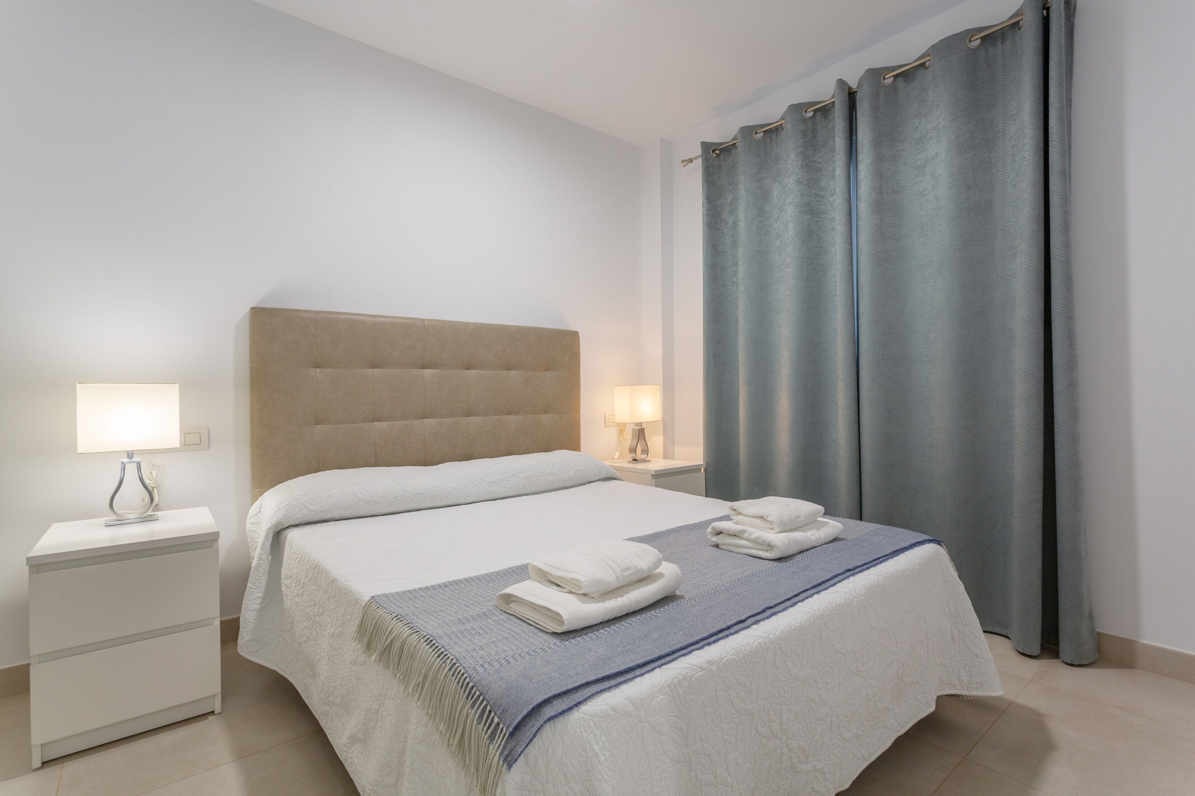 A hotel room with a bed, nightstands, a lamp, a window with curtains, and a towel on the bed.