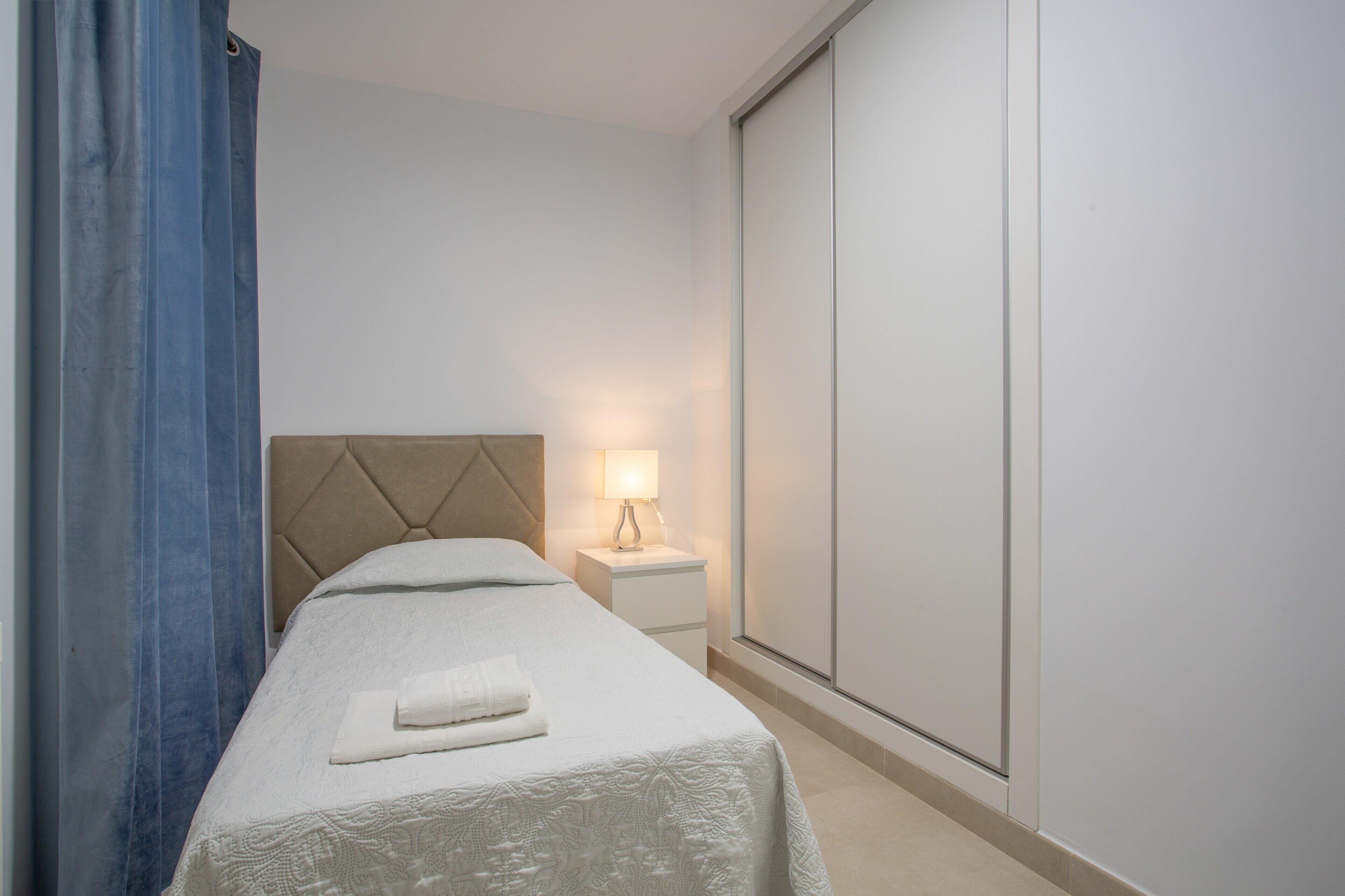 Una habitación de hotel con cama, mesita de noche, lámpara y armario.