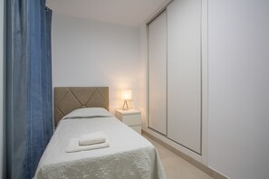 Una habitación de hotel con cama, mesita de noche, lámpara y armario.