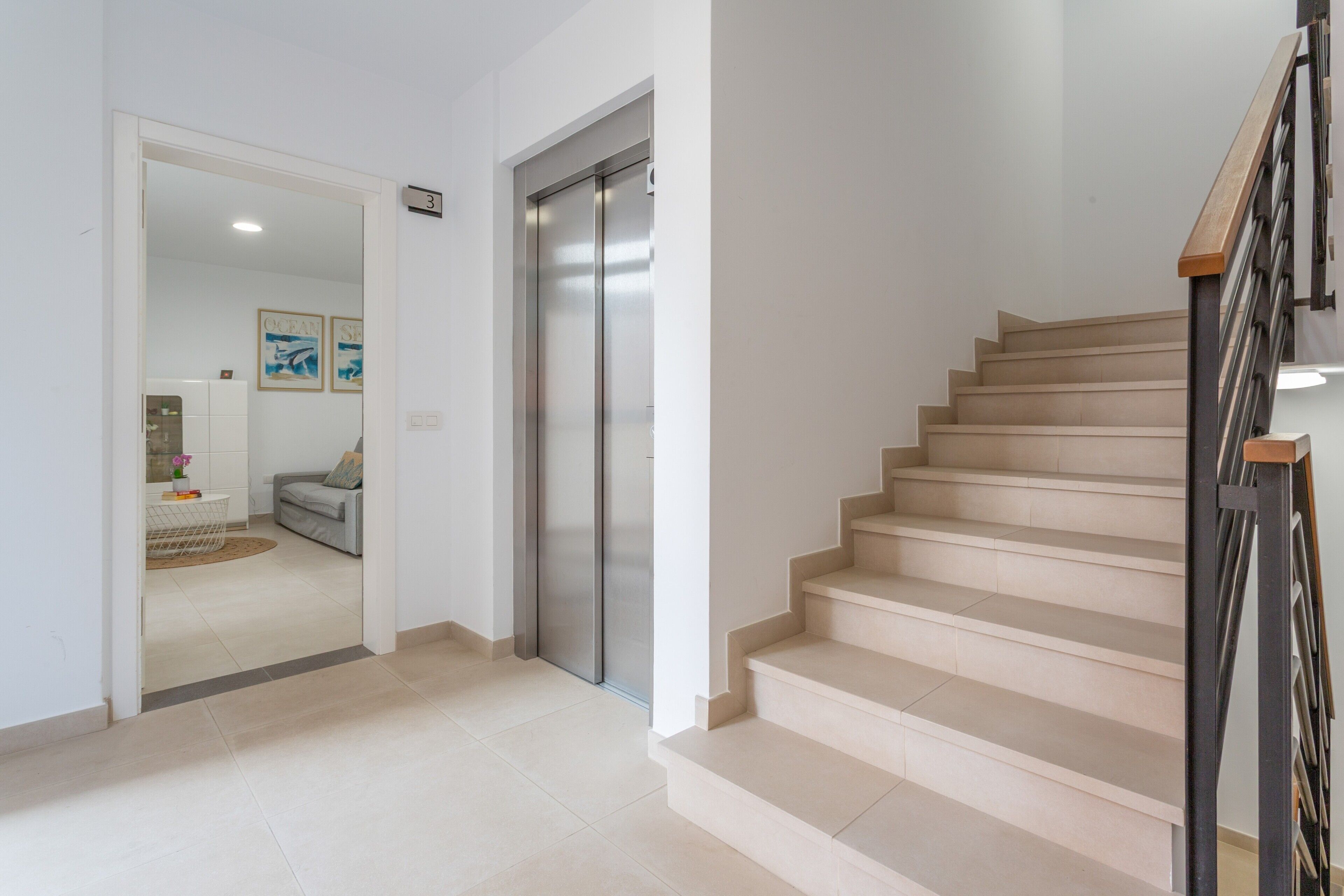 Un interior moderno con una escalera, una puerta que da a un área de estar y un ascensor empotrado en la pared.