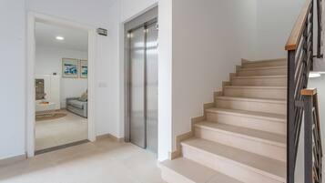 Un interior moderno con una escalera, una puerta que da a un área de estar y un ascensor empotrado en la pared.