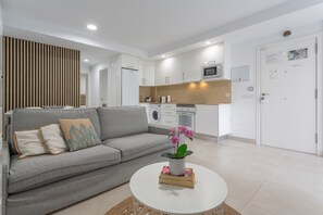Una sala de estar moderna con un sofá gris, una mesita de centro con una planta y una cocina al fondo.