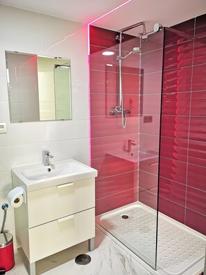 Ein modernes Badezimmer mit einer Duschkabine aus Glas, einem weißen Waschbecken und einem Spiegel.