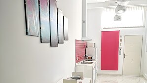 A modern living room with a sofa, a dining table with chairs, a kitchen area with a red door, and artwork on the wall. - Studio Apartment 'Ofis - Estudio Morado' with Wi-Fi and Air Conditioning (Conil de la Frontera)