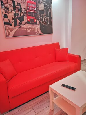 Ein rotes Sofa mit Fernbedienung auf einem weißen Tisch in einem Zimmer, dessen Wand ein Stadtbild zeigt.