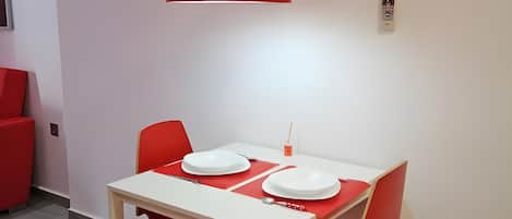 A dining area with a white table and red chairs, a red pendant light, and an air conditioning unit on the wall.