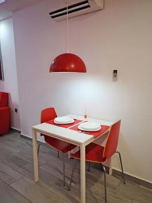 Ein Essbereich mit einem weißen Tisch, roten Stühlen, einer roten Pendelleuchte und einer Klimaanlage an der Wand.