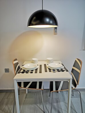 A dining table with four chairs, a black pendant light, and a white tablecloth. - Studio Apartment 'Ofis - Estudio Negro' with Wi-Fi and Air Conditioning (Conil de la Frontera)