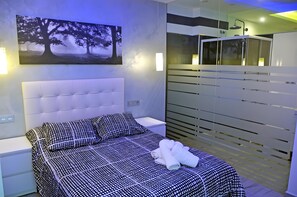 A modern bedroom with a large bed, a nightstand, a wall-mounted TV, and a bathroom with a shower and a mirror. - Studio Apartment 'Ofis - Estudio Negro' with Wi-Fi and Air Conditioning (Conil de la Frontera)