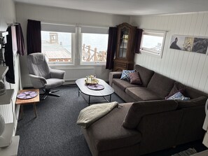 A living room with a grey armchair, a brown sofa, a small coffee table, and a view of the sea through large windows.
