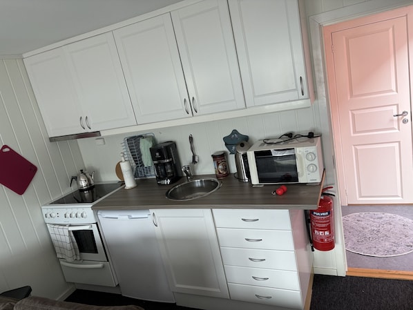 A compact kitchen with white cabinets, a microwave, a coffee maker, and a kettle.