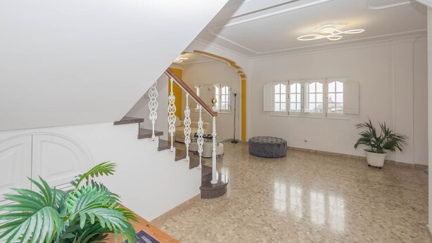 A spacious interior with a polished floor, a staircase with ornate railings, and a large window providing natural light. - 4-Bedroom Villa El Romero—Private Pool, BBQ & Relaxation (Arucas)