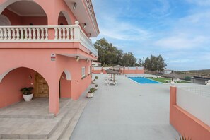 Un bâtiment rose doté d’une piscine, d’un espace extérieur aménagé et d’un escalier menant à l’entrée.