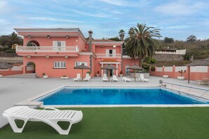 A two-story building with a swimming pool, white lounge chairs, and a palm tree. - 4-Bedroom Villa El Romero—Private Pool, BBQ & Relaxation (Arucas)