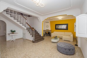A spacious living area with a staircase, a sofa, a coffee table, and a decorative ottoman. - 4-Bedroom Villa El Romero—Private Pool, BBQ & Relaxation (Arucas)