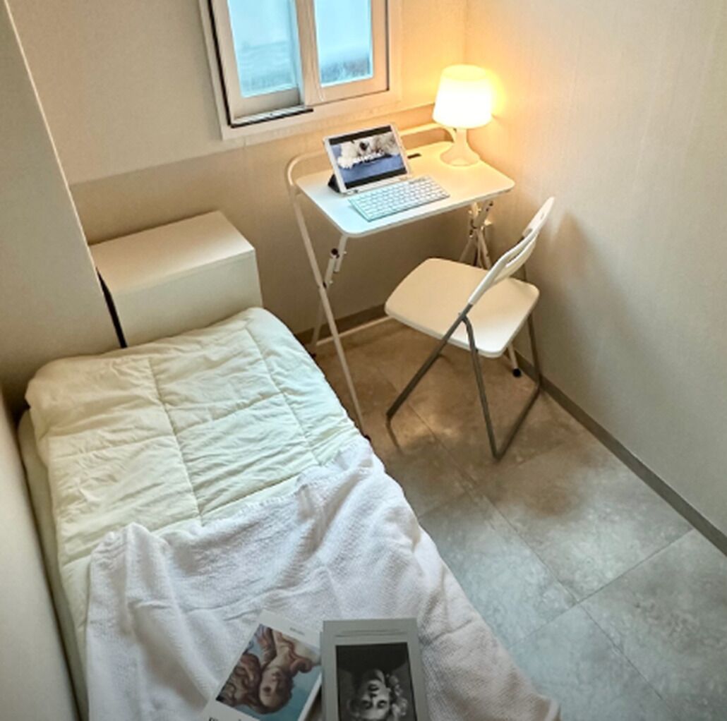 A small, compact room with a bed, a desk with a laptop, and a chair.