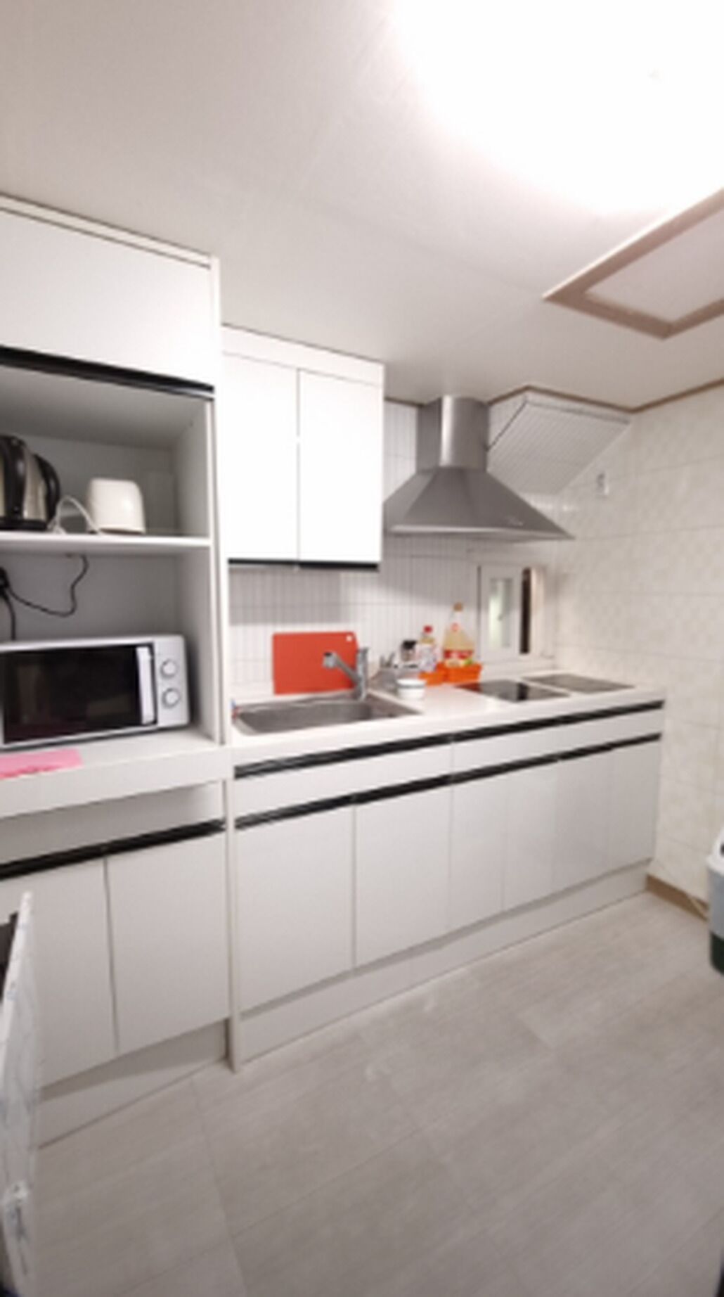 A modern kitchen with white cabinets, a microwave, a red appliance, and a stainless steel range hood.