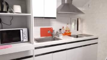 A modern kitchen with white cabinets, a microwave, a red appliance, and a stainless steel range hood.