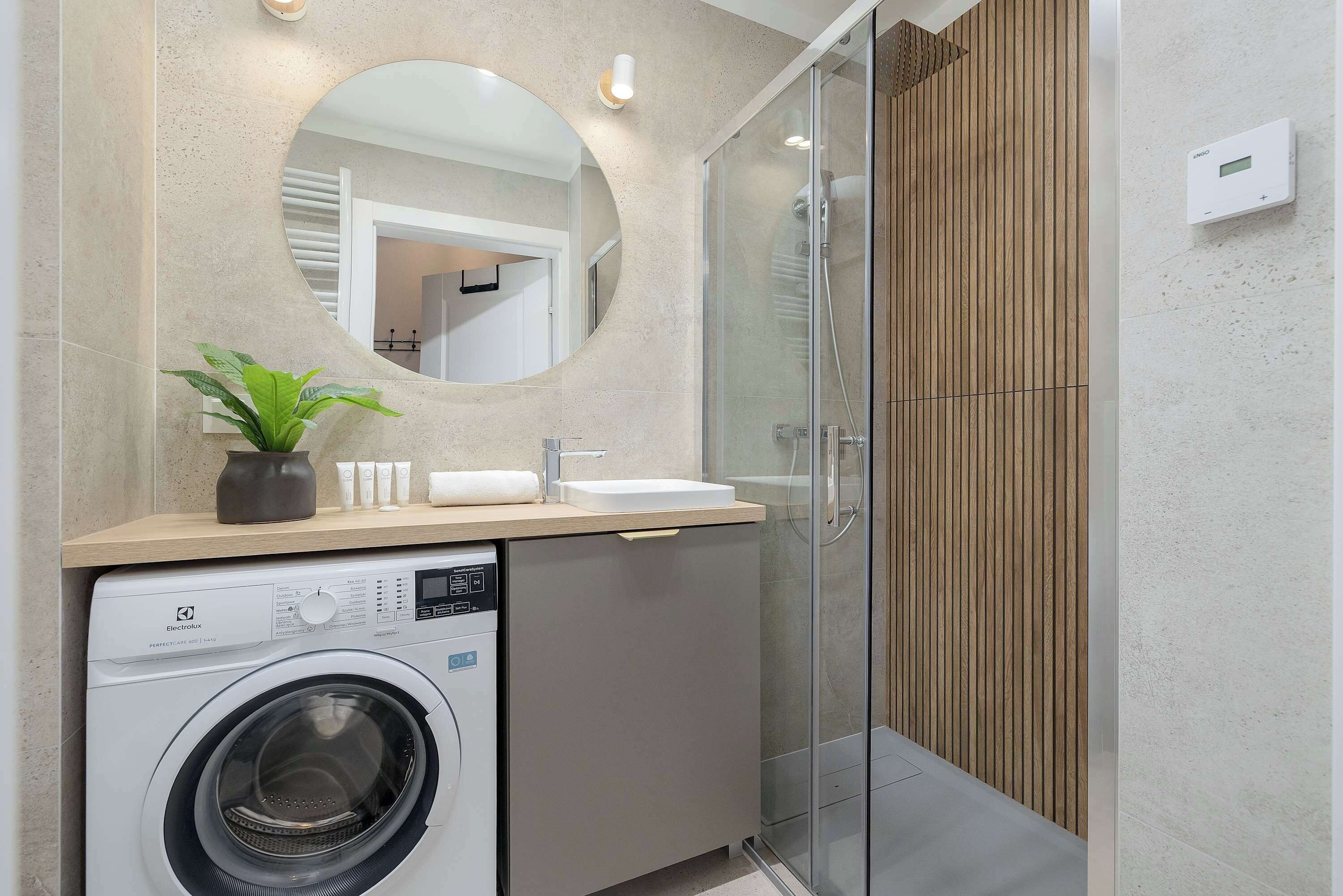 Une salle de bain moderne équipée d’un lave-linge, d’un évier et d’une douche à parois de verre.