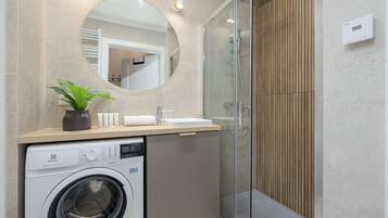 Une salle de bain moderne équipée d’un lave-linge, d’un évier et d’une douche à parois de verre.