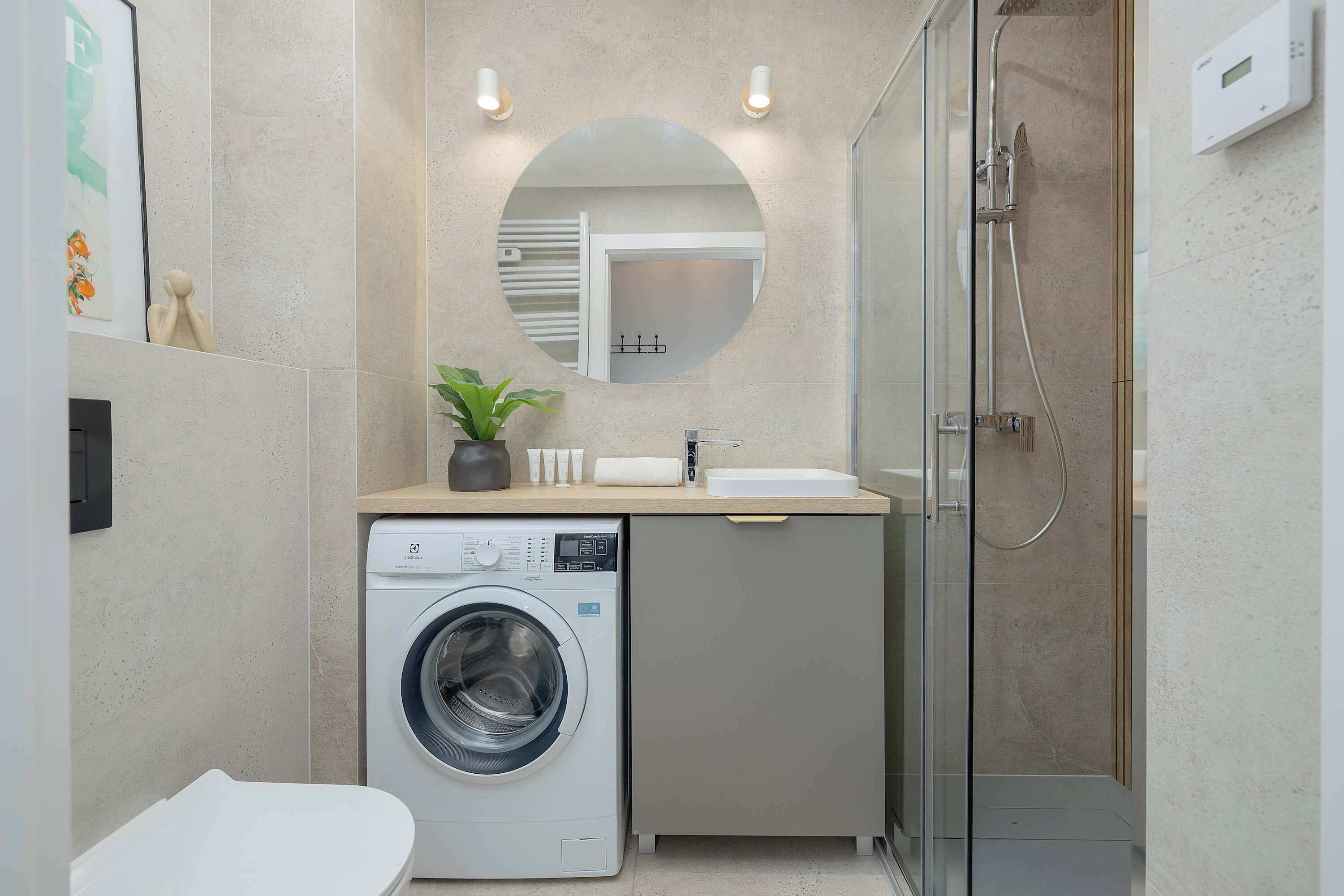 Une petite salle de bain équipée d’un lave-linge, d’un évier et d’une douche.